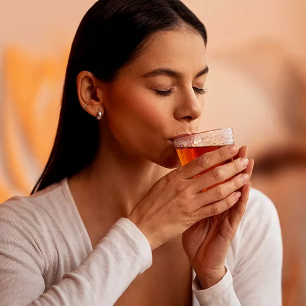 Como parte da experiência do Day Spa calm a foto mostra uma mulher com os olhos fechados, segurando com as duas mãos um copo de vidro com um liquido transparente alaranjado e com a boca encostada no copo