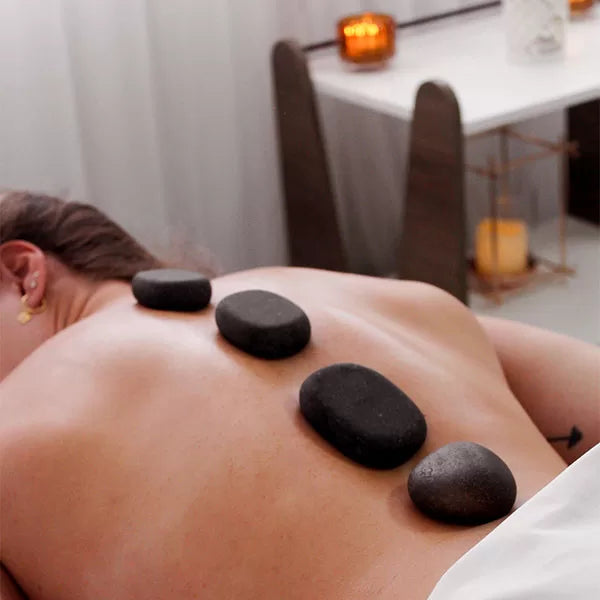 Capa do produto experiência hot stones no speciale spa com a foto mostra as costas de uma mulher e duas mãos segurando em cada uma uma pedra preta, que são pressionadas na altura do ombro da mulher