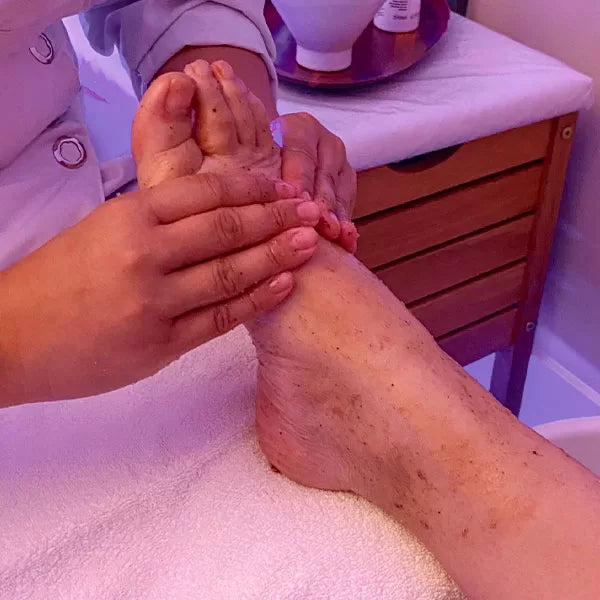 Como parte da experiência spa dos pés a foto mostra um pé apoiados em uma toalha branca sendo massageado por duas mãos