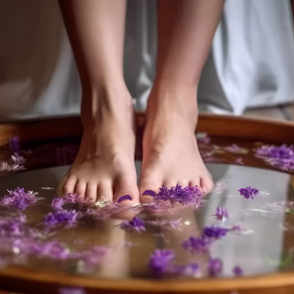 Como parte da experiência do Day Spa calm a foto mostra dois pés submerso na água onde há flores roxas submersas em uma bacia de madeira 