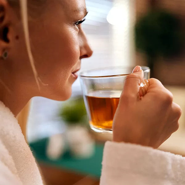 Como parte da experiência do Day Spa essence a foto mostra a lateral do rosto de uma mulher, que segura uma xícara na altura de sua boca com um líquido amarelo dentro