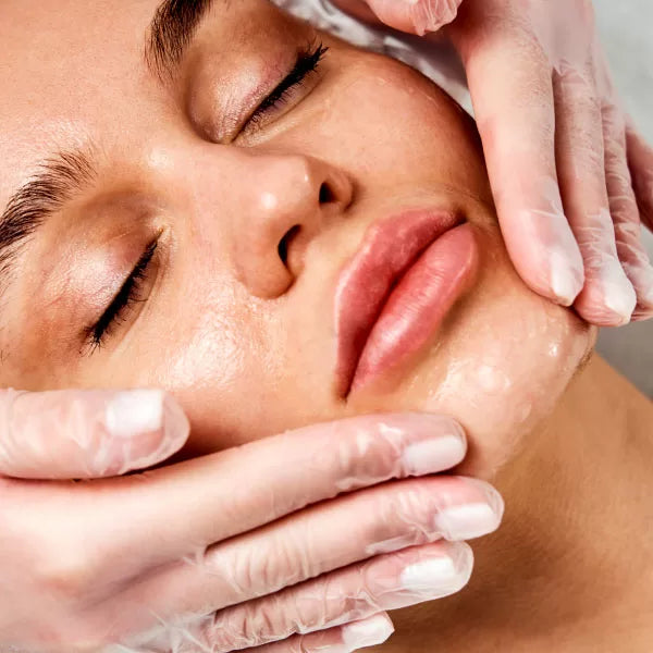 Como parte da experiência do Day Spa amigas a foto mostra o rosto de uma mulher de olhos fechados. Um par de mão está com as pontas dos dedos apoiadas em seu queixo
