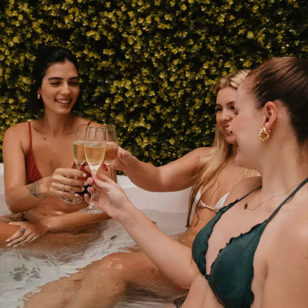 Como parte do produto day spa celebrate a foto mostra três amigas dentro de uma jacuzzi, cada uma segurando uma taça de champagne, sorrindo e brindando