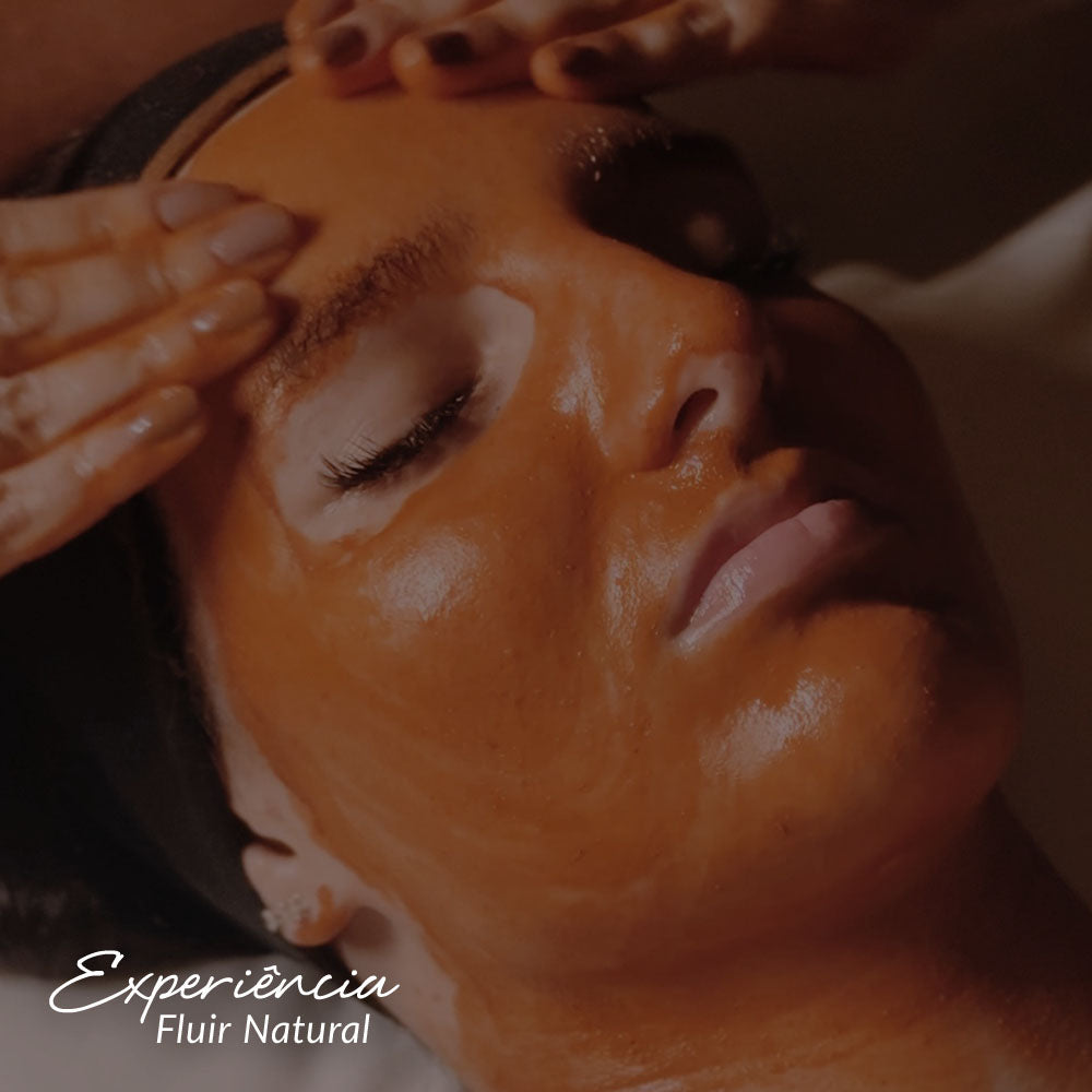 Capa do produto experiência fluir natural com a imagem do osto de uma mulher de olhos fechados. Um creme marrom alaranjado está espalhado em sua face e duas mão estão com os dedos apoiados em sua testa