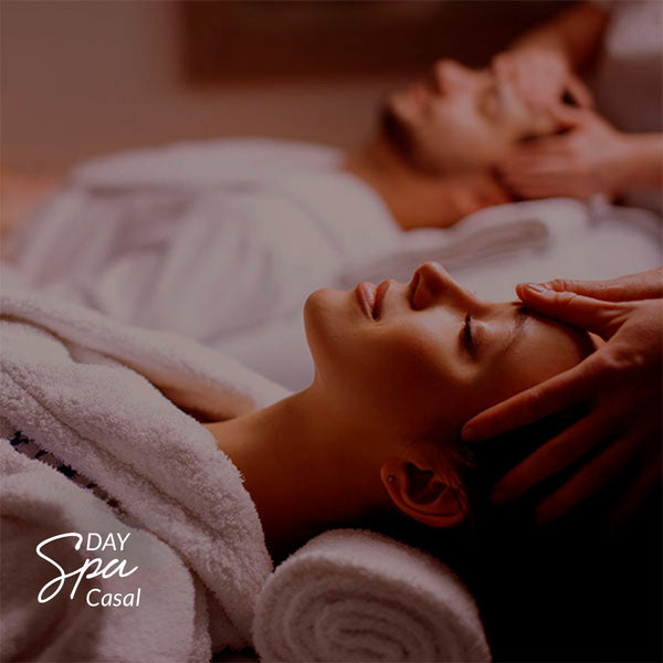 Capa do produto day spa casal no speciale spa representado porum homem e uma mulher, cada um deitado em uma maca, vestindo roupões brancos e recebendo massagem na cabeça. O homem está ao fundo da foto, desfocado, enquanto a mulher está em primeiro plano