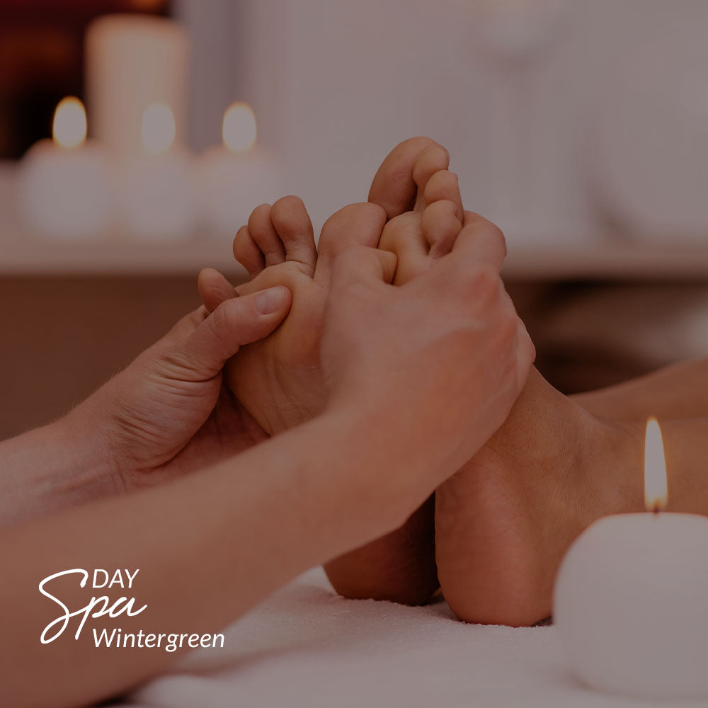 Capa do produto day spa wintergreen no speciale spa representado uma foto de dois pés apoiados na vertical em cima de uma toalha branca. Um par de mão os aperta, com os polegares pressionando no centro de cada pé, abaixo dos dedos. Em volta, há velas acesas