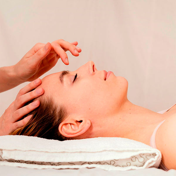 Como parte da experiência do Day Spa wintergreen a foto mostra o lado direito do rosto de uma mulher que está deitada com a cabeça apoiada em um travesseiro branco coberto com uma toalha também branca. Uma mão direita está apoiada no topo da cabeça enquanto a esquerda está suspensa sobre o rosto com o indicador levemente inclinado para o meio das sobrancelhas