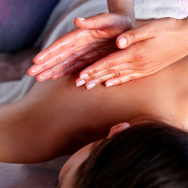 Como parte da experiência do Day Spa wintergreen a foto mostra uma mulher deitada de bruços com a cabeça, que está sendo mostrada parcialmente, voltada para a câmera. Uma toalha branca cobre metade de suas costas.  Duas mãos estão apoiadas nas costas voltadas para o obro da mulhes e com as laterais dos mindinhos voltadas para baixo, fazendo as palmas das mãos ficarem viradas uma para a outra, com a mão direita parcialmente a frente a esquerda