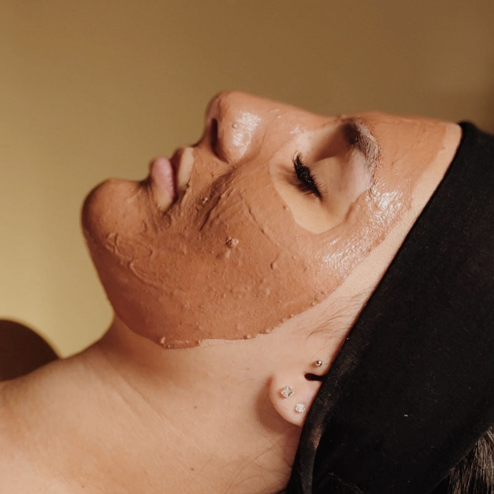 Capa do produto experiência fluir natural com a imagem do osto de uma mulher de olhos fechados. Um creme marrom alaranjado está espalhado em sua face e duas mão estão com os dedos apoiados em sua testa