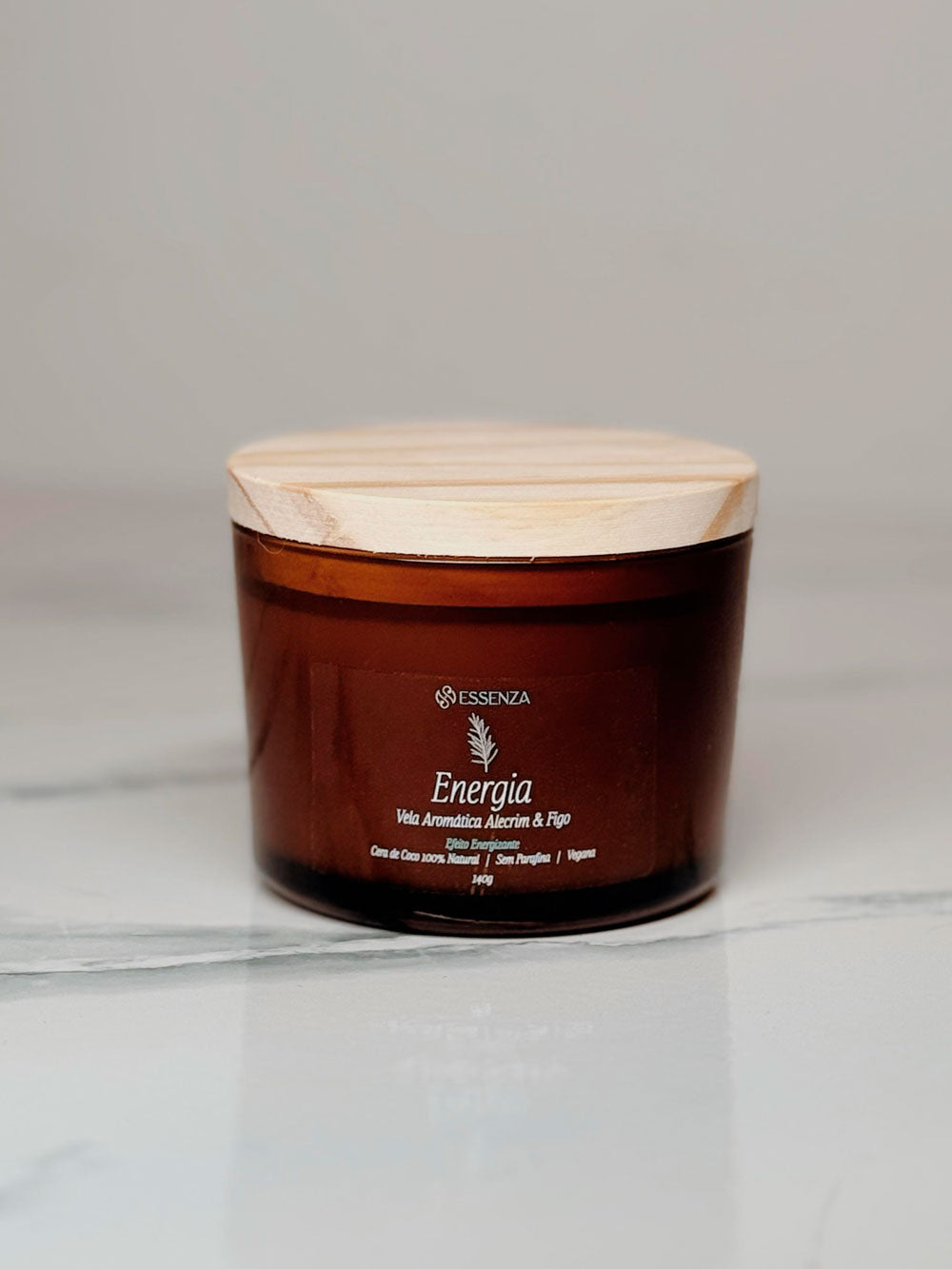 uma embalagem cilindrica de vidro ãmbar com o nome da vela aromática energia, um ramo de alecrim informação do produto estampados. fechado a embalgem há uma tampa de madeira sobre um fundo branco